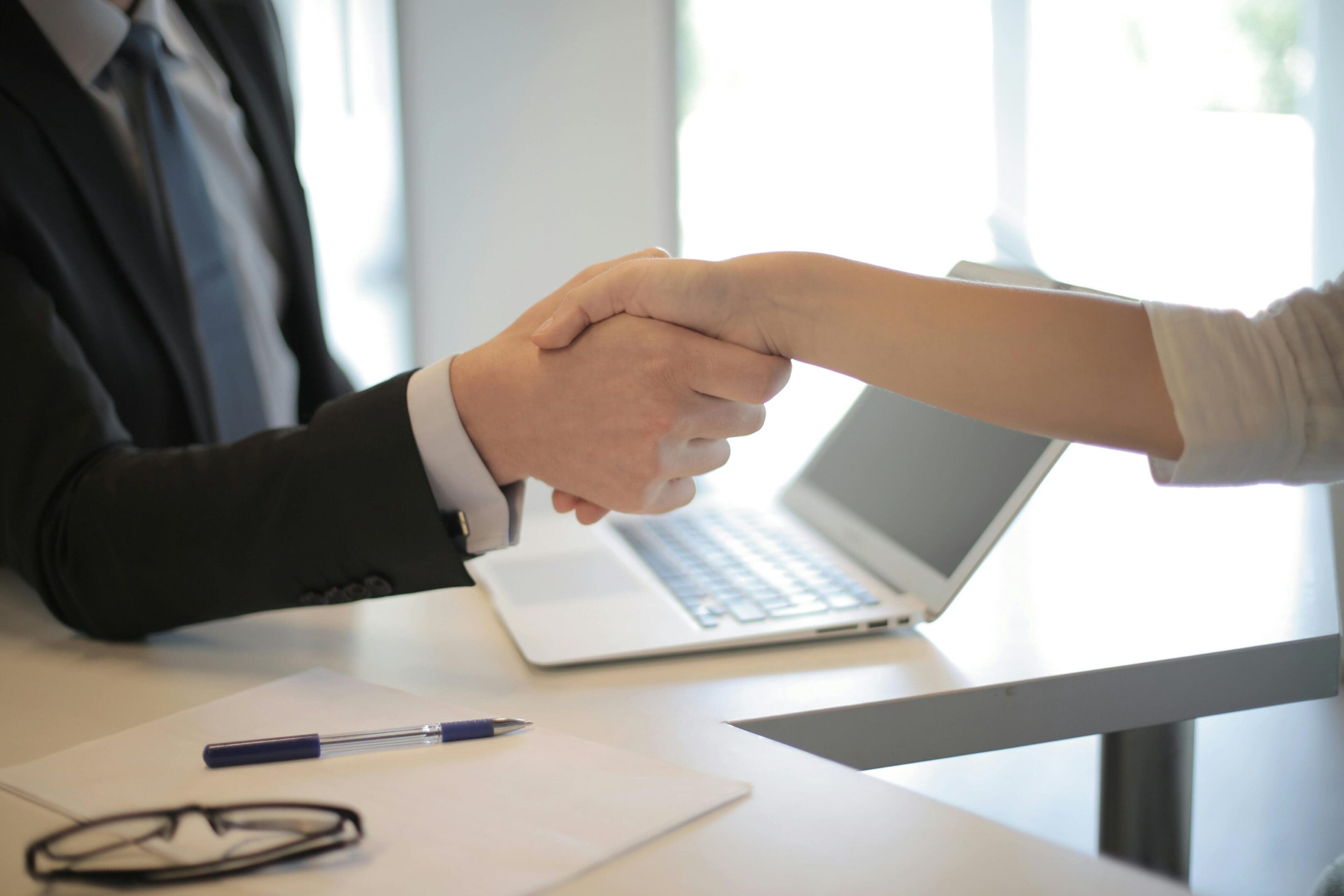 Two people shaking hands over a laptop